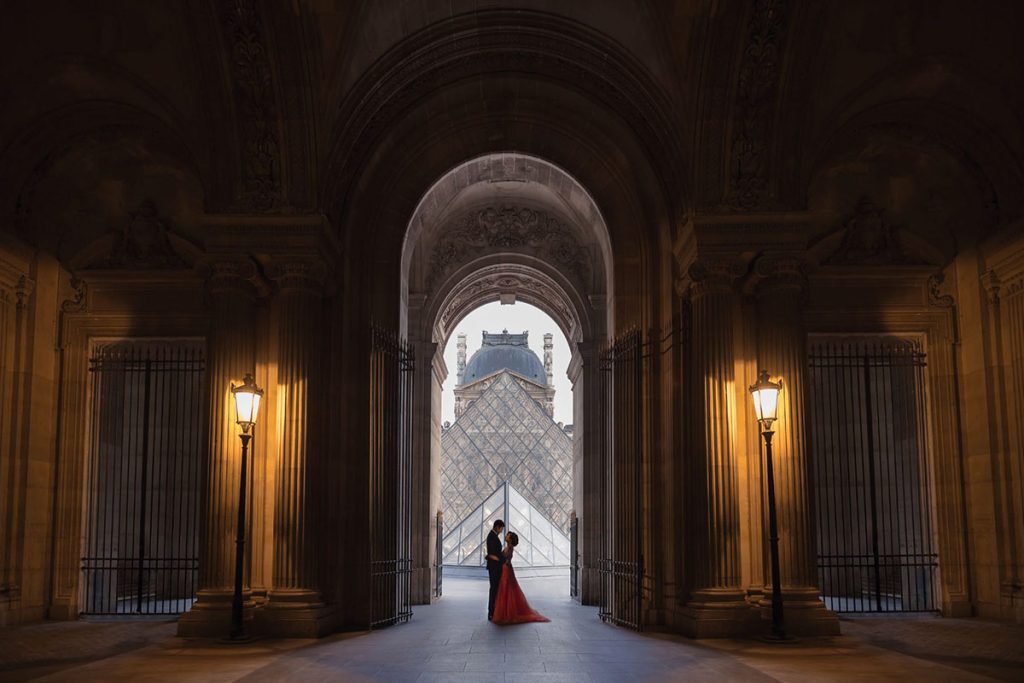 A bride in a red gown and a groom get portraits taken at the Louvre in Paris, France by Emma Wilson from Story of Your Day, Luxury Wedding Videographer