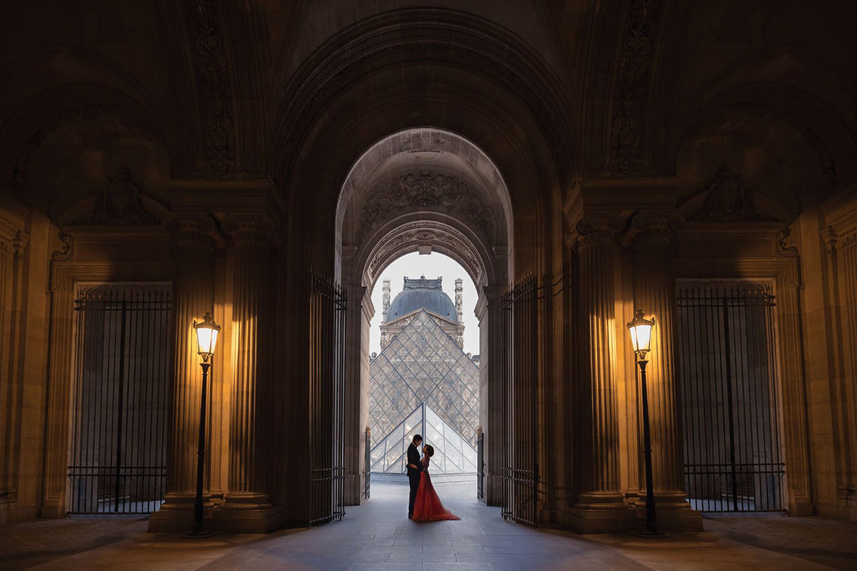 A bride in a red gown and a groom get portraits taken at the Louvre in Paris, France by Emma Wilson from Story of Your Day, Luxury Wedding Videographer