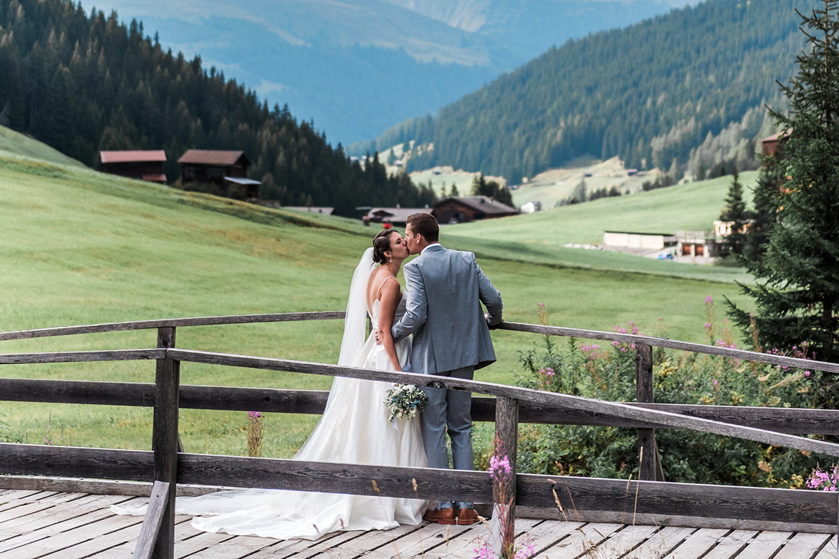 A bride and groom kiss on a wooden bridge in the Sertig Valley on their wedding day