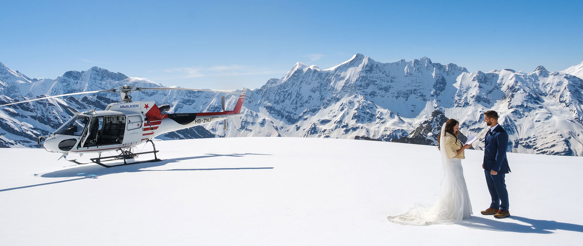 A bride and groom exchange wedding vows standing on a glacier in the Jungfrau region in Switzerland with a helicopter behind them during their Swiss elopement.