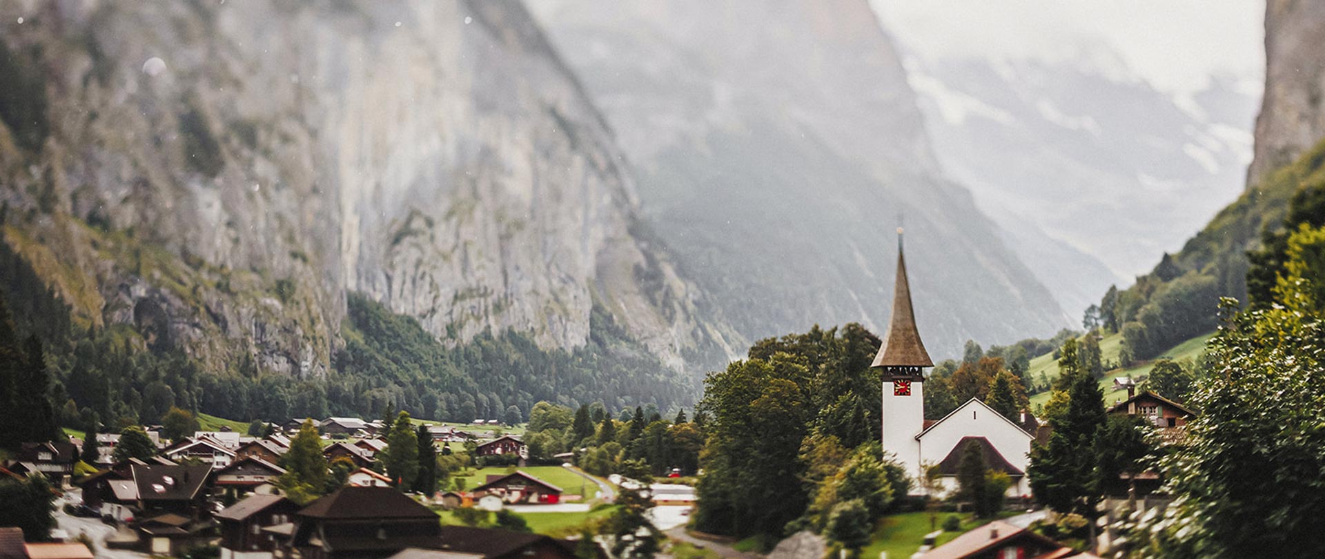 A small village with traditional houses and the iconic Lauterbrunnen church sits in a green valley surrounded by steep rocky mountains.