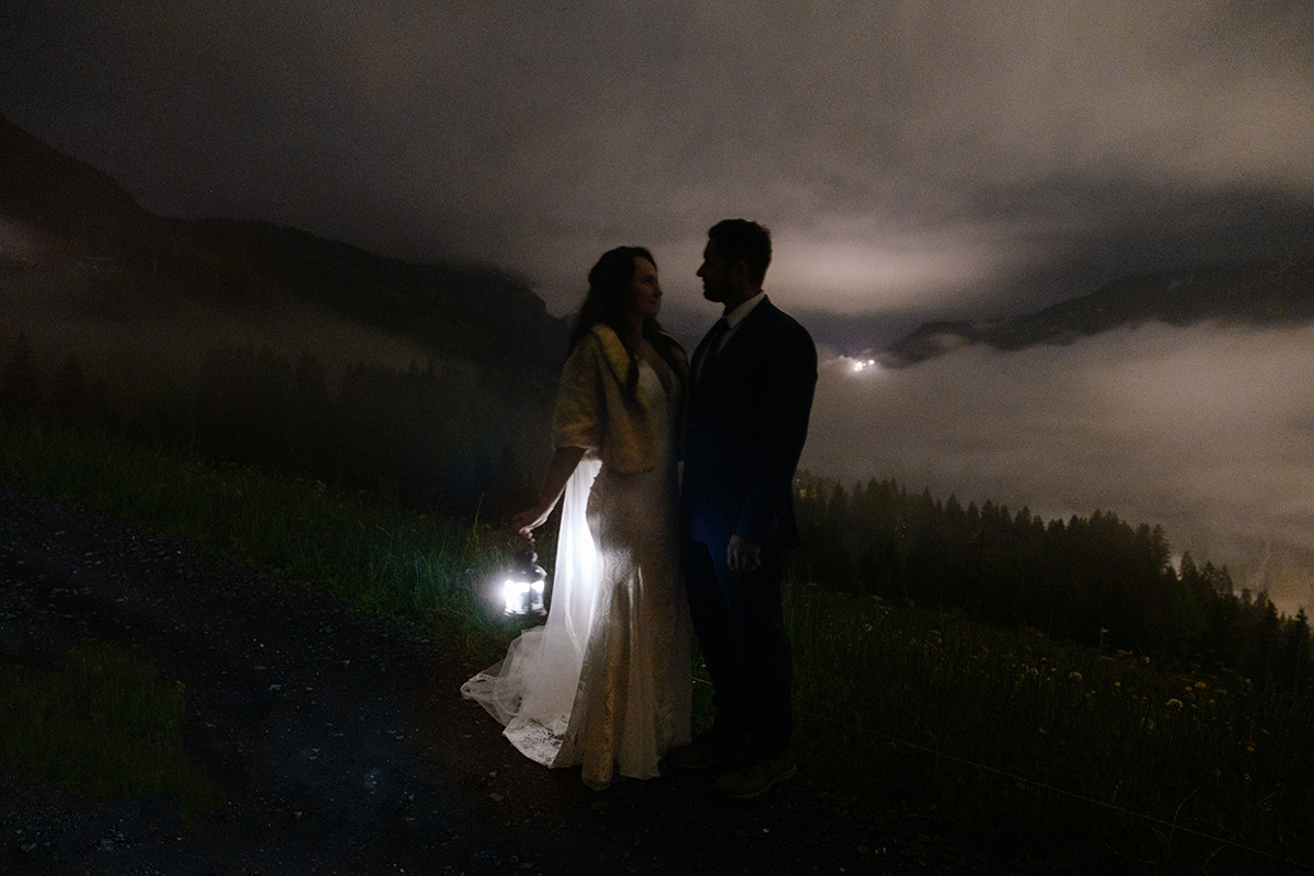 Eloping couple holds a lantern during their nighttime hike in the Swiss alps.