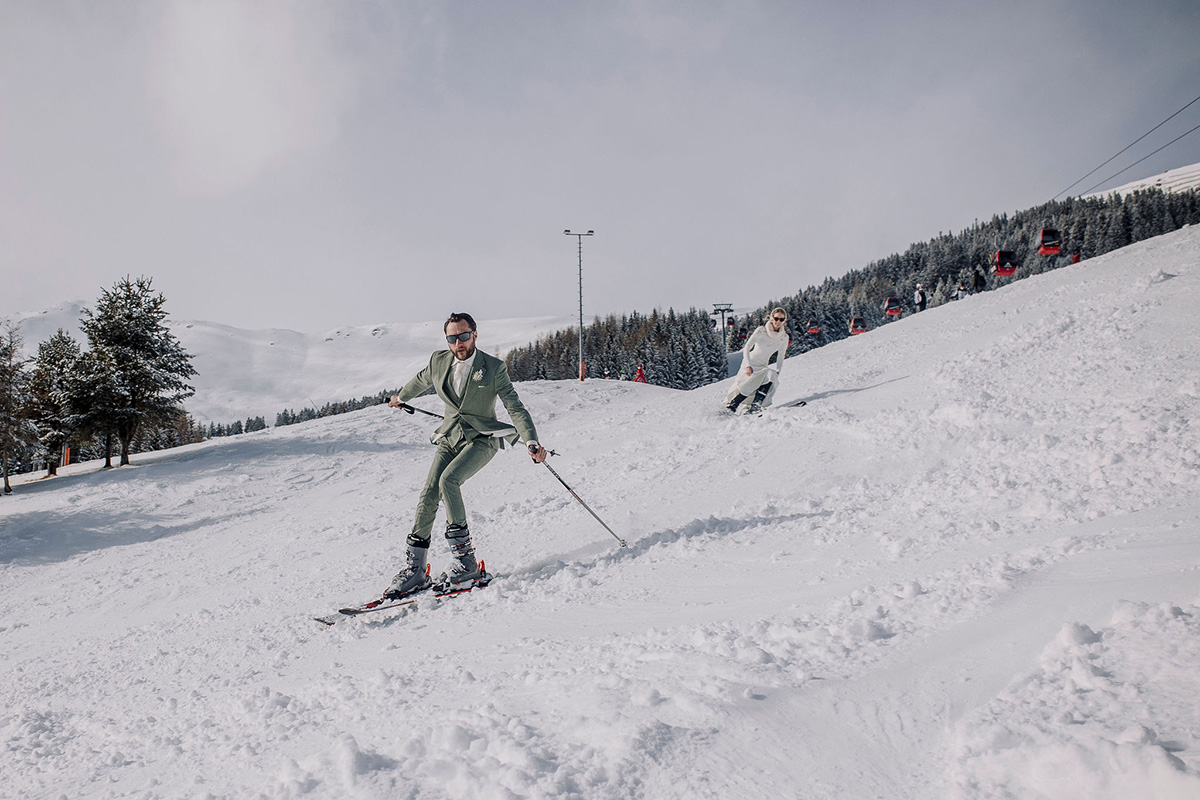 Man in a suit and woman in a white dress ski down a mountain as part of their adventure wedding in Switzerland.