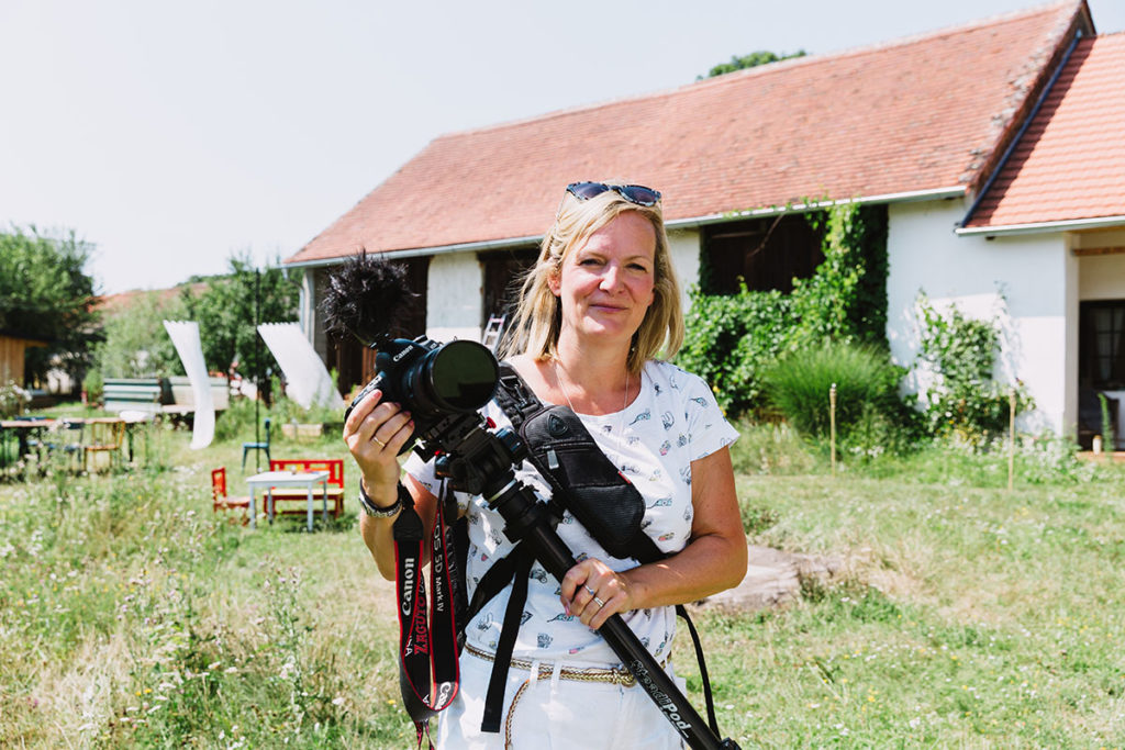 Image of Swiss Wedding Videographer, Emma Wilson, Smiling at the camers holding her camera and tripod