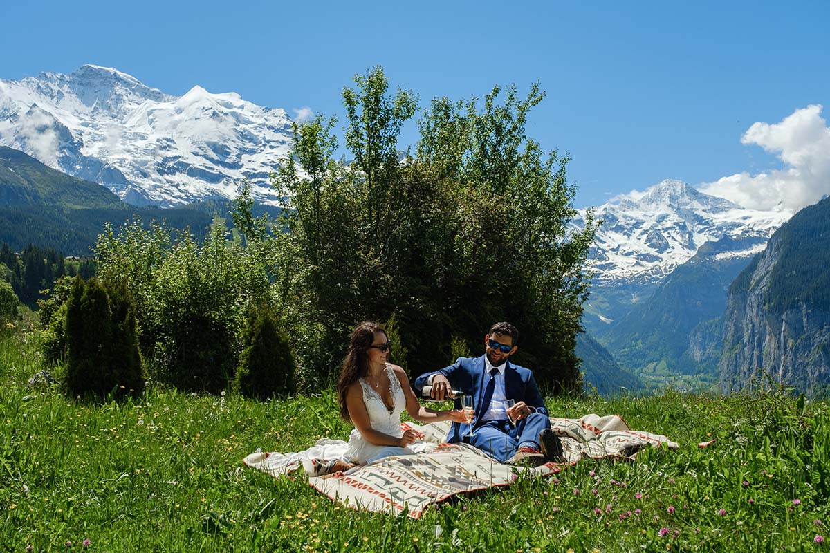 A bride and groom sit on a blanket in a field in Wengen with the Jungfrau behind them during their Swiss Adventure elopement