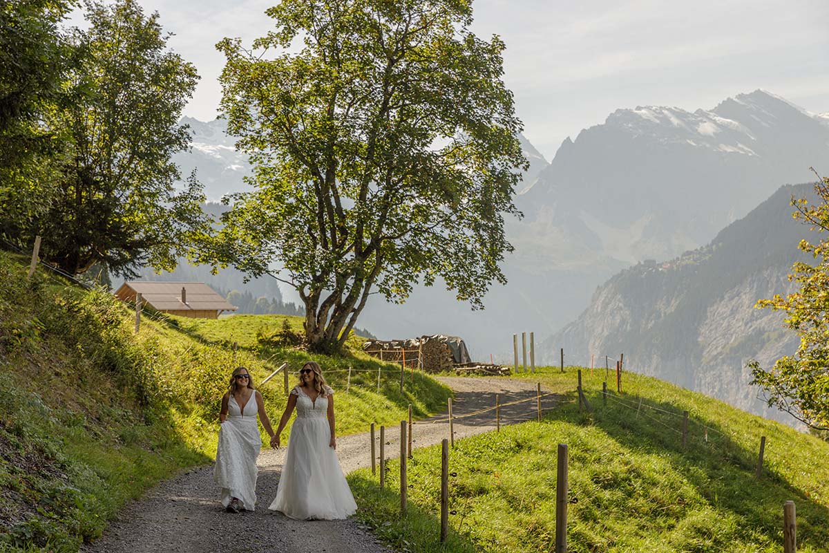 Two Brides walk hand in hand along a path in farmland above Wengen during their elopement portrait session