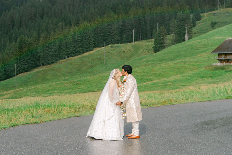 A couple kissing at their wedding with a rainbow in the background by Emma Wilson from Story Of Your Day