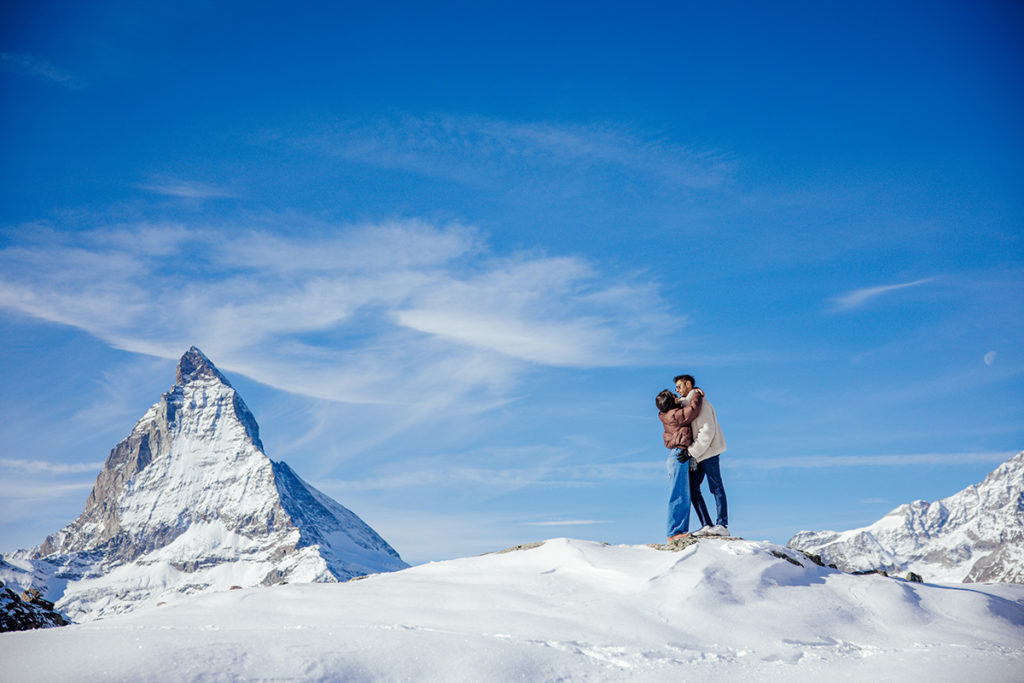 A couple embraces on a snowy hill with the Matterhorn mountain in the background, capturing the magic of a destination Engagement shoot in Zermatt