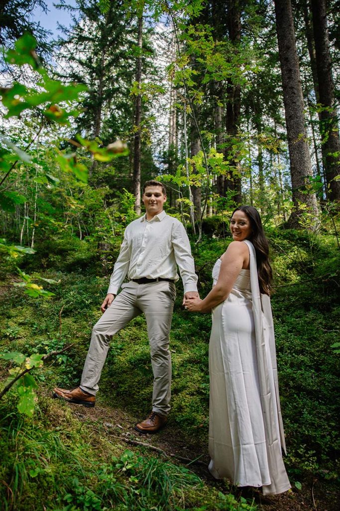 A man and woman holding hands stand on a forest path surrounded by green trees and foliage in Wengen, Switzerland during their Proposal.
