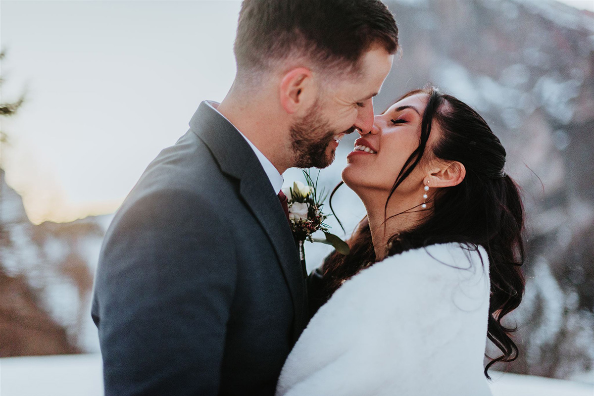 A couple dressed in formal attire embrace and smile at each other outdoors in a snowy, mountainous setting, perfectly captured by an adventure wedding videographer. Story Of Your Day