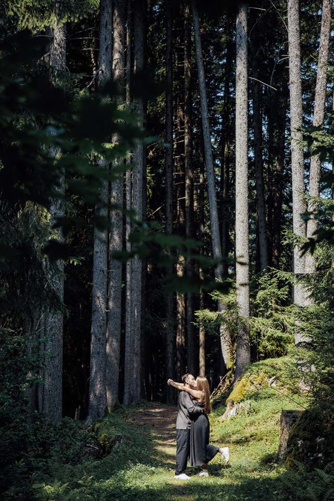 Two people embracing on a sunlit forest path in Lauterbrunnen Valley, surrounded by tall trees and dense greenery—a magical spot for a heartfelt proposal Wengen.