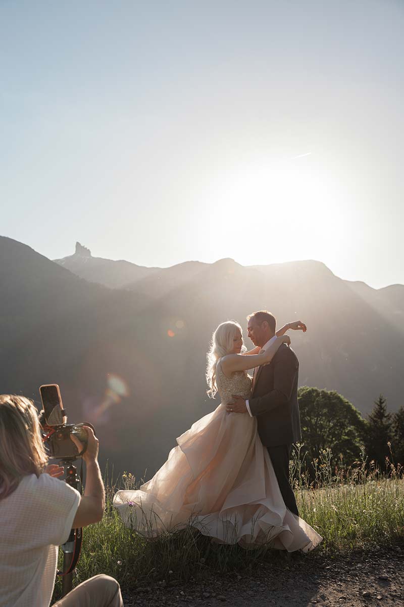 A photographer captures a bride and groom embracing outdoors at sunset, with mountains and sunlight in the background—perfect inspiration for your elopement page.
