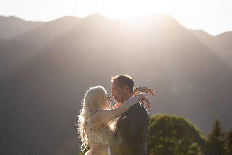 A couple dressed in wedding dress and suit embrace outdoors at sunset, mountains and trees silhouetted behind them in the hills above Wengen.