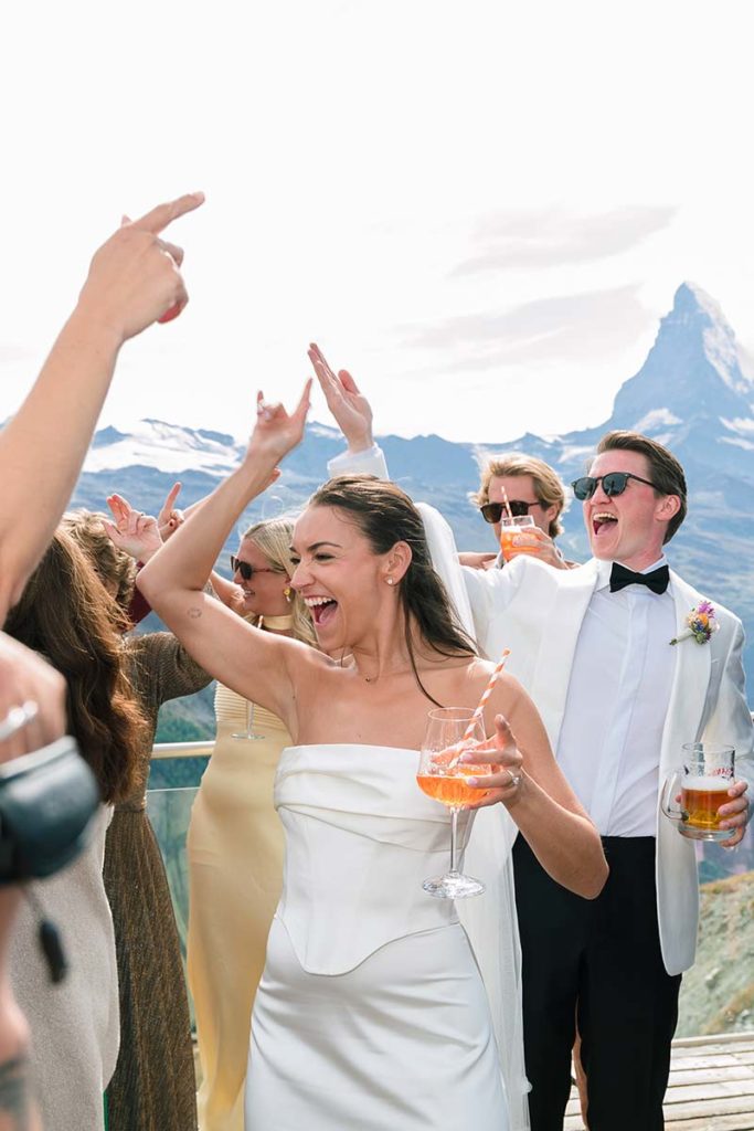 A bride in a white dress and a groom in a tuxedo dancing with guests in Switzerland in front of the Matterhorn.