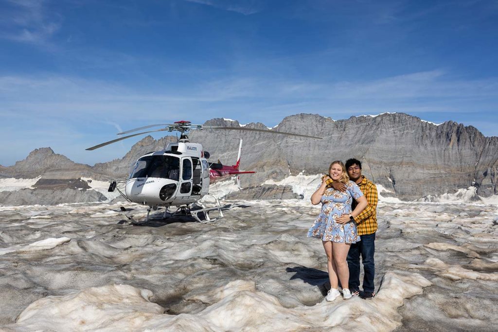 A couple poses in front of a helicopter on a snowy Swiss mountain glacier, captured by a wedding filmmaker.