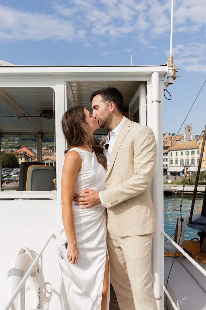 A couple in wedding attire kiss on the deck of a boat, captured by a Switzerland wedding filmmaker.