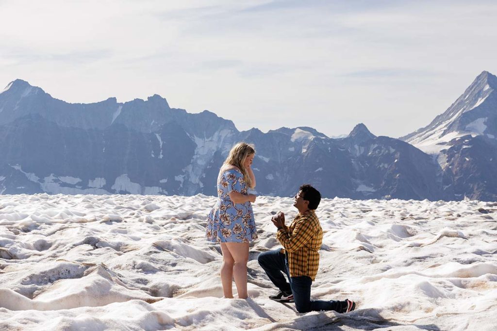 A man kneeling to propose to a woman in a stunning Switzerland wedding landscape.
